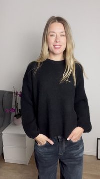 Black knitted sweater with long sleeves, relaxed fit, and crew neckline, paired with dark jeans, set against a neutral background.