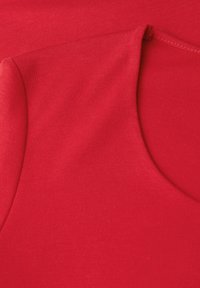 Czerwony materiał ukazujący zbliżenie gładkiej struktury, z okrągłym dekoltem i detalami szwów, podkreślający dopasowany krój.