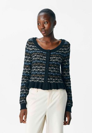 Cardigan noir avec un motif de tricot complexe, comportant des accents bleus, bruns et blancs, un col rond, une fermeture à boutons et un ourlet froncé.