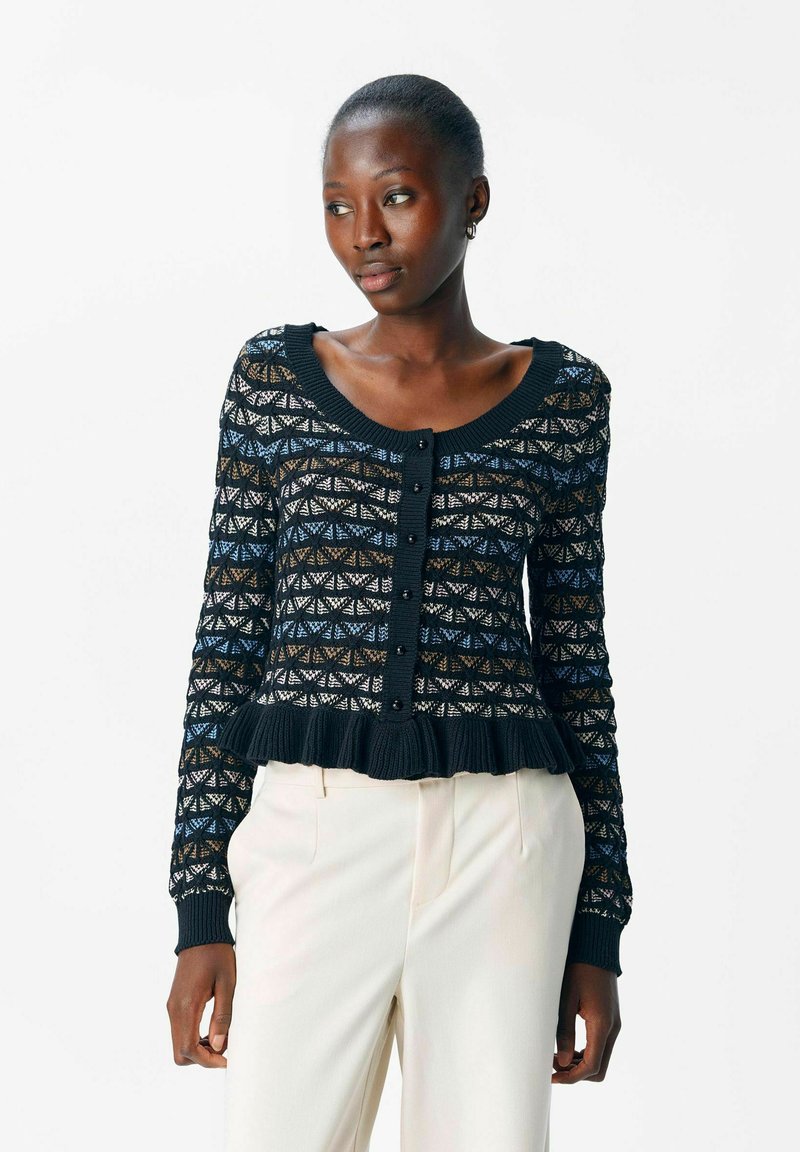 Cardigan noir avec un motif de tricot complexe, comportant des accents bleus, bruns et blancs, un col rond, une fermeture à boutons et un ourlet froncé.