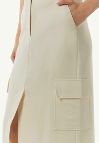 Cream-colored skirt with a side slit, featuring a patch pocket and smooth, textured fabric. Seam detail near the pocket adds subtle interest.