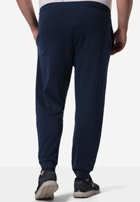 Marineblaue Jogginghosen mit weicher Textur, schmalem Schnitt und elastischem Bund. Sie verfügen über Seitentaschen und Rückentaschen-Details. Kombiniert mit dunklen Sneakers.