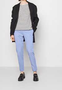 Czarny długi płaszcz, paskowany biało-granatowy top, jasnoniebieskie spodnie i czarne mokasyny z złotym akcentem.