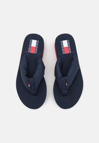Navy flip-flops with padded upper straps, featuring a Tommy Jeans logo in navy, red, and white on the footbed. Textured rubber sole.