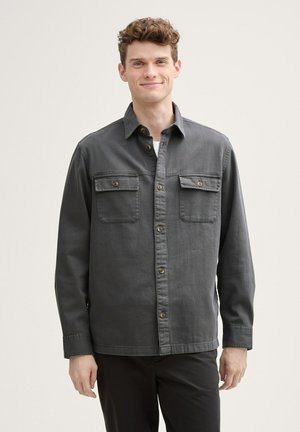 Camisa de botón gris oscuro hecha de una mezcla de algodón, con dos bolsillos en el pecho, cuello y dobladillo recto.