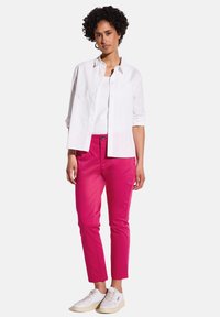 Chemise blanche à boutons sur un débardeur blanc, assortie à un pantalon slim rose et des baskets blanches. La tenue présente un design décontracté.