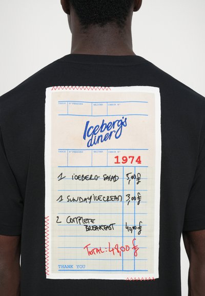 Schwarzes T-Shirt mit einem großen, genähten Patch, der wie eine Quittung aus einem Diner aussieht, mit blauer und roter Schrift, die Lebensmittel und Preise auflistet.