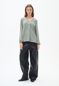Blusa a maniche lunghe di colore verde chiaro con scollatura a V e davanti plissettato, abbinata a pantaloni in pelle nera larghi. Tessuto morbido e voluminoso.