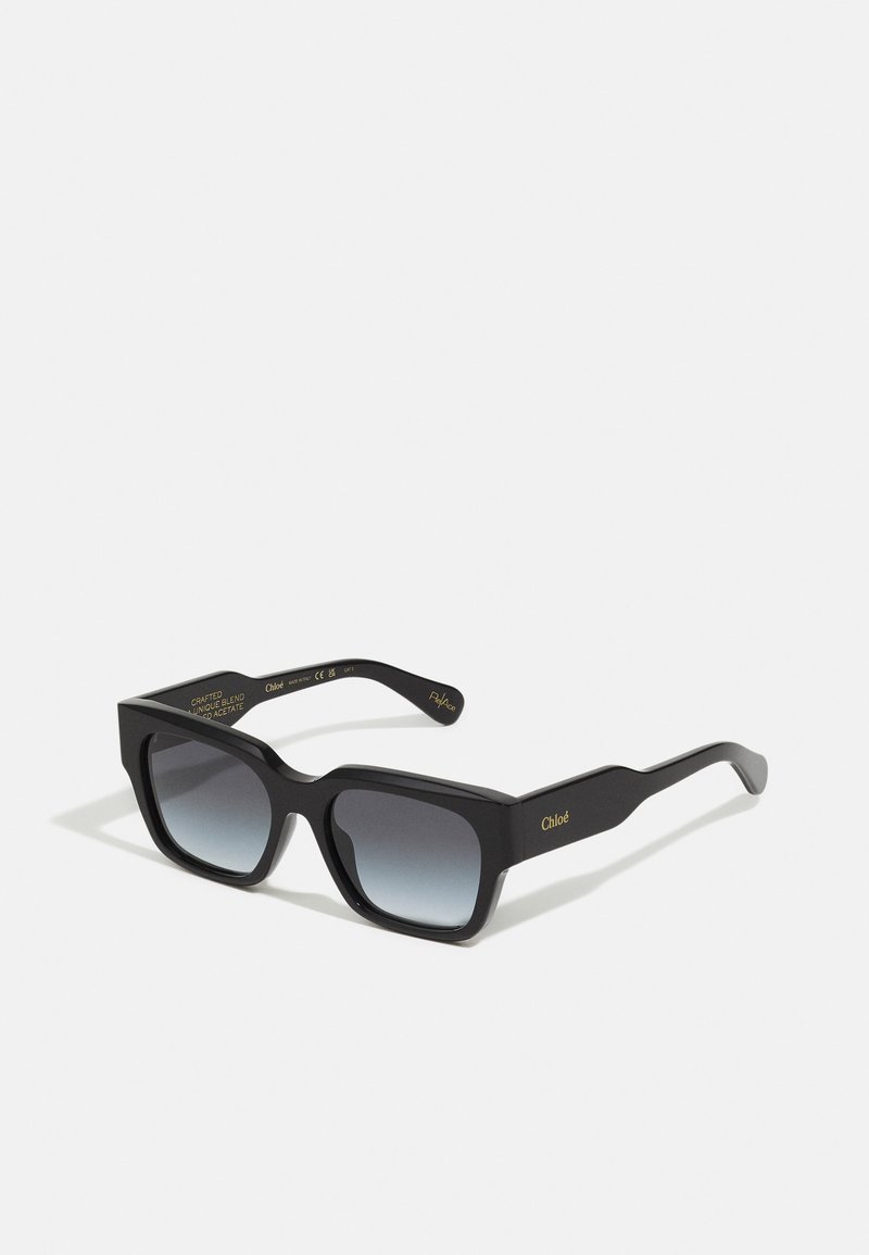 Black acetate sunglasses with a bold square frame, gradient lenses, and gold branding inside the temples. Features a textured finish.