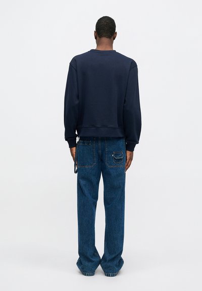 Mörkblå sweatshirt med nedhasade axlar och ribbad muddar, i kombination med löst sittande mörkblå jeans med bakficka och sidodetalj.