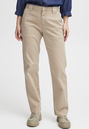 Beige rechte broek met ceintuurlussen, gedragen met beige chunky sneakers en een donkerblauwe blouse met lange mouwen.