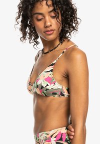 Bikini top s cvetnim vzorcem, ki ima trikotno obliko, nastavljive naramnice in kontrastne barve roza, zelena in črna.