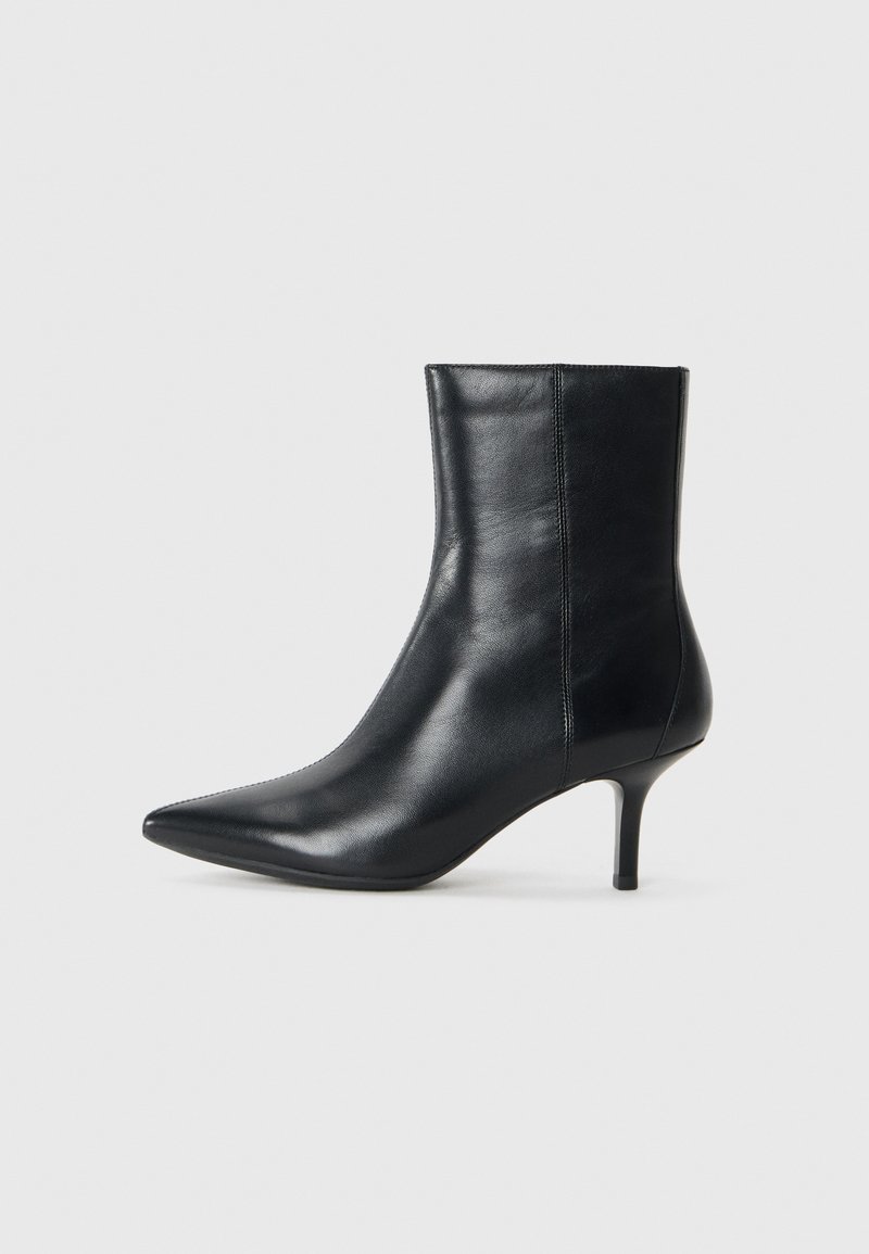 Svart läderankelboot med spetsig tå, smal klack, slät yta och minimal sömdetaljering. Klassisk design som passar till olika outfits.