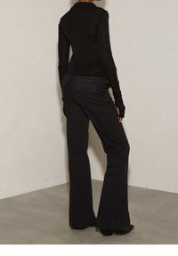 Maglietta nera a maniche lunghe e pantaloni neri svasati con una finitura testurizzata. L'outfit presenta un sottile design della tasca posteriore e maniche aderenti.