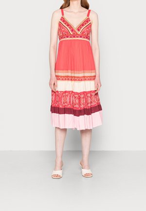 Femme portant une robe sans manches multicolore, longueur genou, avec des motifs floraux et rayés, et des sandales blanches à bouts ouverts.