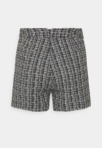 Shorts en tweed noir et blanc avec un motif texturé, une taille ajustée et une fermeture éclair au dos. Forme rectangulaire, longueur mi-cuisse.