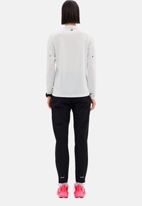Langärmliges, hellgraues Sportoberteil mit Rundhalsausschnitt, kombiniert mit schwarzen Hosen und leuchtend pinken Sportschuhen. Minimalistisches Design, reflektierende Akzente.