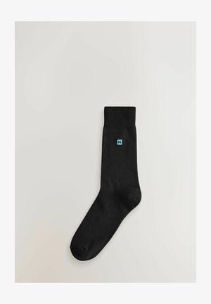 Melna zeķe, kas izgatavota no gludas auduma ar ribotu apkakli. Sānos ir neliels zils logo formas burtam 'N'.