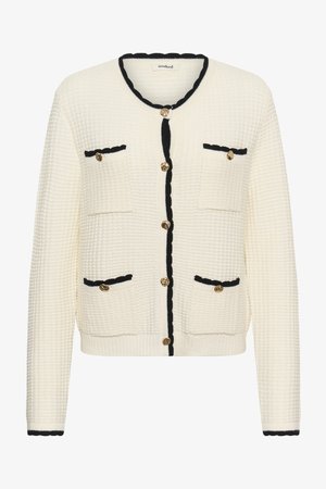 Fehér strukturált kötött kardigán fekete szegéllyel, hat arany gombbal, és négy zsebbel az elején, fekete szegélyű fedőlapokkal és gombokkal.