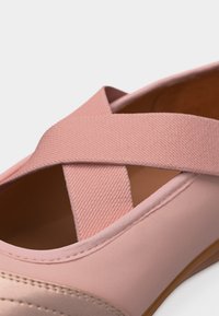 Ροζ μπαλαρίνες με ελαστικούς υφασμάτινους λουράκια που διασταυρώνονται και λεπτομέρειες από λείο ράψιμο στο πάνω μέρος.