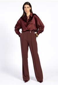 Bordeaux satijnen blouse met een kraag, gecombineerd met hoge, wijde broek in een bijpassende tint. Gladde textuur en minimale hardware-details.