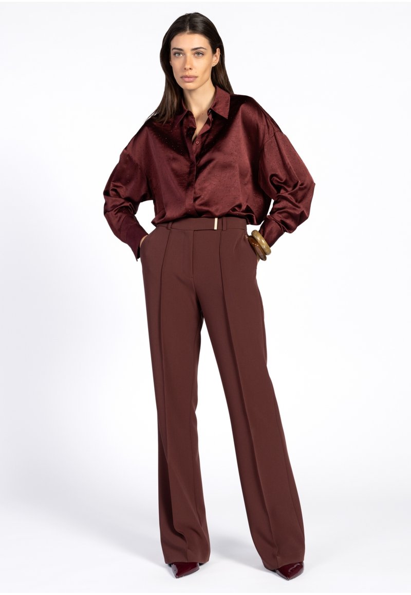 Bordeaux satijnen blouse met een kraag, gecombineerd met hoge, wijde broek in een bijpassende tint. Gladde textuur en minimale hardware-details.