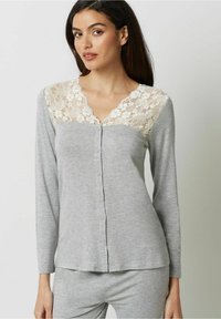 Tricou gri cu mânecă lungă, cu detalii din dantelă la guler, având un închizător cu buton și o textură moale și netedă. Asortat cu o pereche de pantaloni corespunzători.