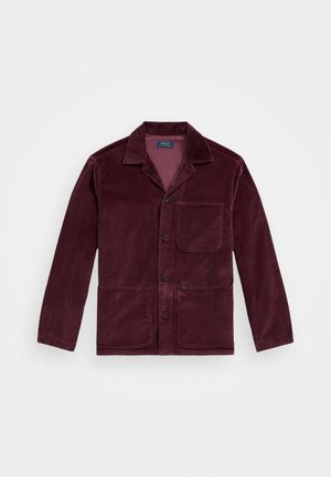 Veste en velours côtelé bourgogne avec un col cranté, fermeture à boutons sur le devant, poche poitrine et deux poches inférieures. Texture lisse avec des côtes visibles.