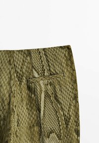 Pantalons à motif serpent vert avec une texture lisse, un design épuré et une poche arrière. Le matériau imite la peau de reptile.