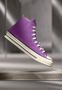 Purple high-top sneaker made of synthetic material, featuring white laces, a rubber toe cap, and black stripes on the sole.