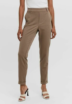 Pantaloni beige su misura con una texture liscia, vestibilità slim, orli arrotolati e dettagli di cucitura in rilievo, abbinati a sandali col tacco bianchi.