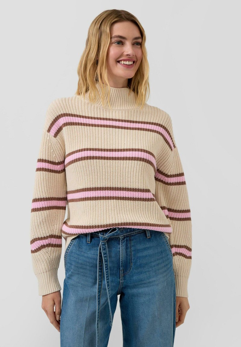 Kremowy sweter z dzianiny w poziome paski w kolorze brązowym i różowym. Posiada wysoki kołnierz i luźny krój, zestawiony z niebieskimi, wysokim stanem jeansami.