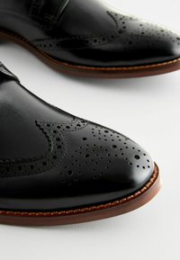 Zapatos de vestir de cuero negro con detalles de brogue, puntera afilada, suela de cuero marrón cosida y acabado pulido que exhiben acentos perforados.