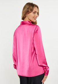 Camicia di raso fucsia con maniche lunghe, colletto classico e polsini abbottonati, caratterizzata da una texture liscia e una vestibilità leggermente ampia.