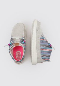 Zapatos de lona beige con tejido de patrón tribal multicolor en los laterales, suelas de goma blanca y plantillas rosas. Presenta cuentas decorativas en los cordones.
