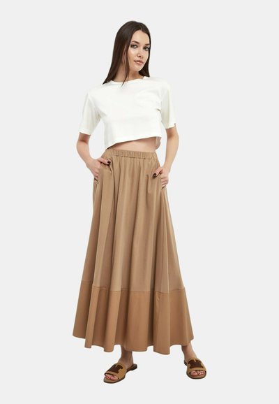Top bianco cropped con maniche corte, abbinato a una gonna maxi plissettata beige a vita alta con tasche e una texture liscia.