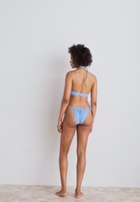 Light blue bikini set featuring a halter-neck top and adjustable ties at the back, with minimal coverage and soft fabric texture.