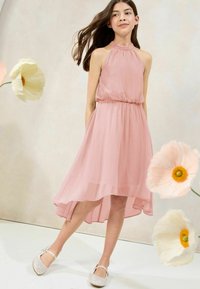 Abito rosa senza maniche con collo all'americana e vita elastica, caratterizzato da un orlo asimmetrico e un tessuto leggero e trasparente. Scarpe bianche scintillanti.