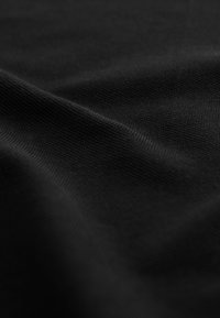 Primer plano de textura de tela negra con un patrón tejido suave y pliegues delicados que crean sombras y reflejos sutiles.