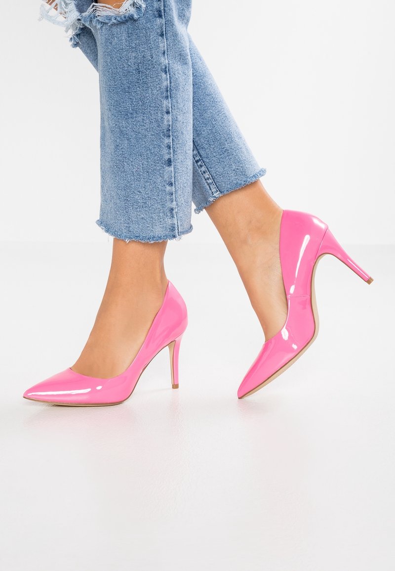 Escarpins en cuir verni rose avec un bout pointu et un talon fin. Le design présente une texture lisse et brillante ainsi qu'un style minimaliste.
