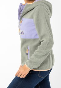 Chaqueta de forro polar con capucha en verde y lila, que cuenta con un bolsillo frontal con cremallera, tejido texturizado y acentos en naranja contrastante en los puños.