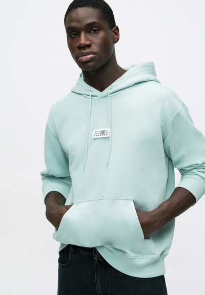 Hellgrüner Kapuzenpullover aus weichem Stoff mit einer Fronttasche, Kordelzügen und einem kleinen Logolabel auf der Brust.