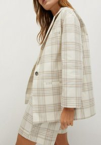 Blazer en tartan crème avec des lignes marron et bleues, doté d'une fermeture à un seul bouton et de poches latérales, associé à un short assorti.