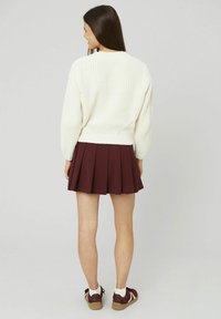Un pull blanc en maille côtelée à manches longues, associé à une jupe plissée bordeaux. Des baskets blanches avec des semelles marron complètent le look.