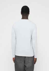 Pika varrukaga valge T-särk ümar kaelusega, valmistatud pehmest puuvillamaterjalist, kantud koos hallide teksapükstega, minimalistliku disainiga, ühtlase tekstuuriga.