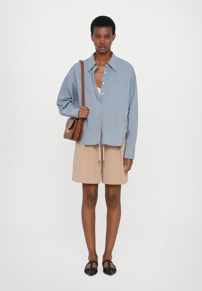 Blaue Chambray-Übergröße mit Knopfleiste, beigefarbene Shorts mit Kordelzug, schwarze flache Schuhe, braune Schultertasche, glatte Textur, lockere Passform.