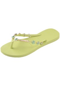 Light yellow flip-flop with textured footbed, V-shaped straps adorned with flowers and metallic accents, and a logo on the strap.
