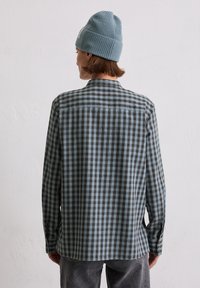 Long-sleeve shirt in black and light blue checkered pattern, with a button-down collar and visible stitching. Paired with a light blue beanie.