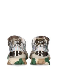 Zapatillas con un talón metálico y brillante, parte superior estampada en tonos beige y marrón, y una suela tipo camuflaje con acentos en verde y marrón claro.