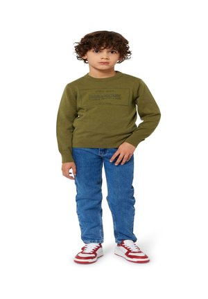 Pull vert avec un col rond et des détails de logo, accompagné d'un jean bleu et de baskets rouge et blanches. Tissu texturé, coupe décontractée.